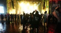 Metal-Fans feiern spät in der Nacht auf dem Festivalgelände des Wacken Open Air (WOA) vor einer Bühne.