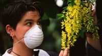 Eine junge Frau schützt sich durch eine Feinstaubmaske vor den Pollen des Goldregens, am 01.01.2000. (Symbolbild)