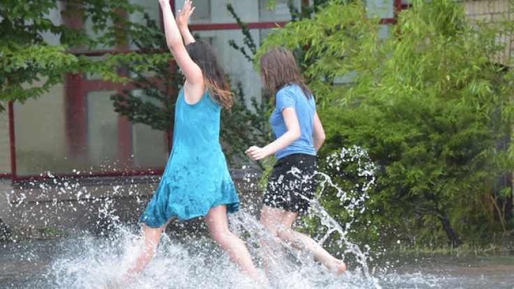 Zwei junge Frauen springen am 22.07.2017 durch vom Regen überschwemmte Wege in Hennigsdorf (Brandenburg).