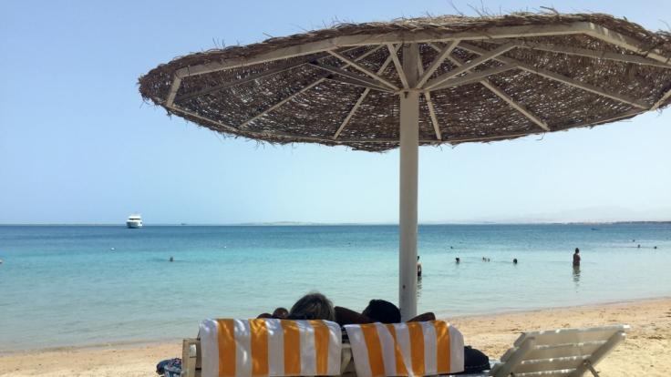 Eine Frau und ein Mann entspannen in Liegestühlen unter einem Sonnenschirm an einem öffentlichen Strand im ägyptischen Hurghada. Vor wenigen Tagen wurden in dem beliebten Urlaubsort zwei tote Hotelgäste aufgefunden.