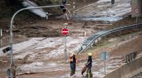 Feuerwehrmänner ziehen einen Schlauch über die verschlammte Bundesstraße 265.