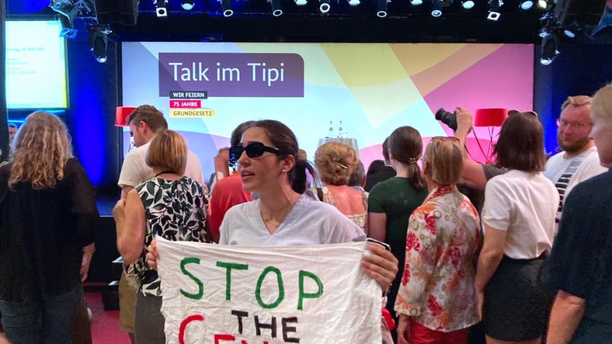 "Stop the Genocide" steht auf einem Transparent, das eine Frau w&auml;hrend des Tipi-Talks mit Au&szlig;enministerin Baerbock in die Kamera h&auml;lt. &nbsp; (Foto)