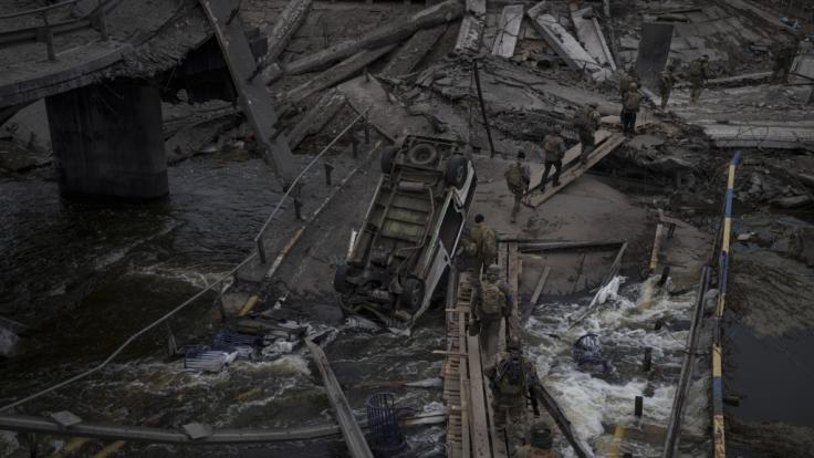 Ausländische und ukrainische Soldaten überqueren einen improvisierten Weg unter einer zerstörten Brücke in Irpin nordwestlich von Kiew.