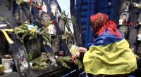 Eine Frau, die in eine ukrainische Flagge gehüllt ist, stellt Blumen und eine Kerze vor das Foto eines Gefallenen am Ehrentag der Hundert Himmlischen Helden.