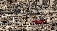 Ein rotes Auto fährt an Häusern und Fahrzeugen vorbei, die durch das Palisades-Feuer in den Pacific Palisades Bowl Mobile Estates zerstört wurden.