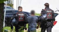 Zwei Einsatzkräfte der Polizei führen vor der Polizeiinspektion einen Tatverdächtigen ab.