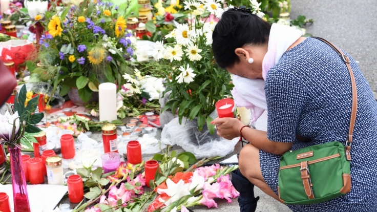 Vor dem Olympia-Einkaufszentrum in München: Eine Frau kniet weinend vor Kerzen und Blumen.