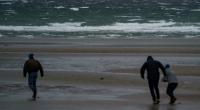 Spaziergänger stemmen sich gegen Windböen vor dem vom Wind aufgepeitschten Wasser am Ostsee-Strand. Der Deutsche Wetterdienst DWD warnte vor Sturm am Wochenende.
