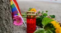 Eine Regenbogenflagge, Blumen und Kerzen stehen vor einem Baum nahe dem Bereich, wo ein Fahrzeug einen Baum gerammt hatte.