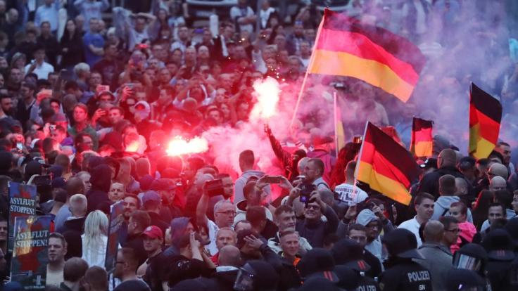 Demonstranten der rechten Szene zünden Pyrotechnik und schwenken Deutschlandfahnen.