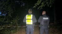 Polizisten stehen an einem abgesperrten Waldstück zwischen Halle-Kölkebeck und Hesselteich, einem Ortsteil von Versmold. Spaziergänger hatten in dem Waldstück im Kreis Gütersloh eine Leiche gefunden.