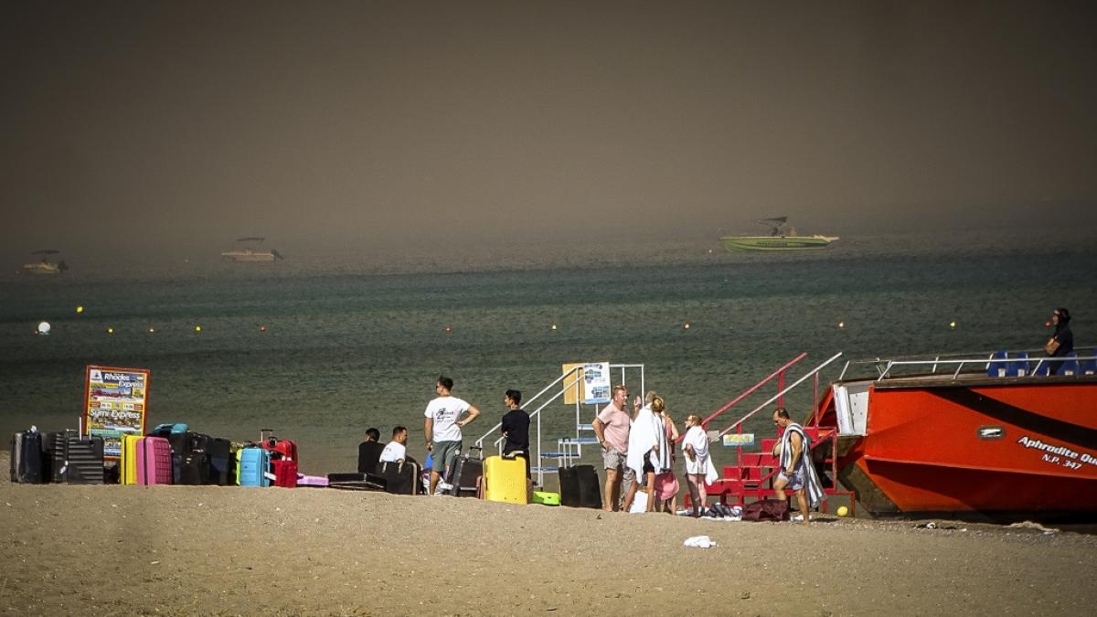 Touristen stehen an einem Strand, wohin sie wegen eines Waldbrandes auf der griechischen Insel Rhodos in Sicherheit gebracht worden sind. (Foto)