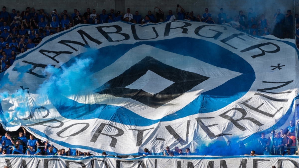 Unter ihrem blauen Wappen feuern die Fans des Hamburger SV ihren Verein an. (Symbolbild) (Foto)