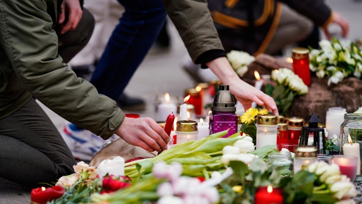 Menschen legen vor einem Geb&auml;ude der Universit&auml;t Blumen und Kerzen an den Wegesrand. (Foto)