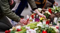 Menschen legen vor einem Gebäude der Universität Blumen und Kerzen an den Wegesrand.