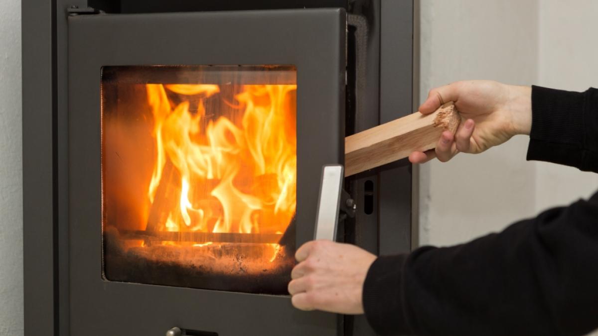 Ein Mann legt in seiner Wohnung ein St&uuml;ck Holz in einen Kaminofen (Symbolbild) (Foto)