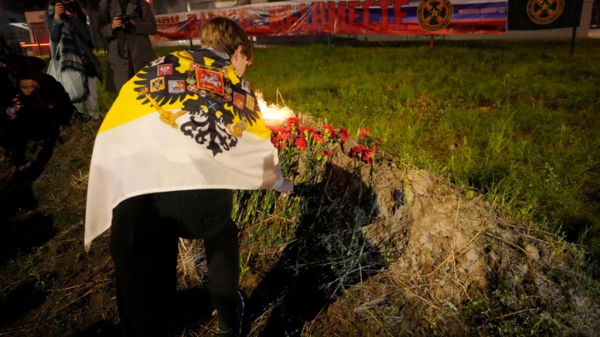 Ein Mann legt Blumen an einer informellen Gedenkst&auml;tte neben dem ehemaligen "PMC-Wagner-Zentrum" ab, w&auml;hrend im Hintergrund ein Banner mit der Aufschrift "PMC Wagner, wir sind zusammen" zu sehen ist. (Foto)