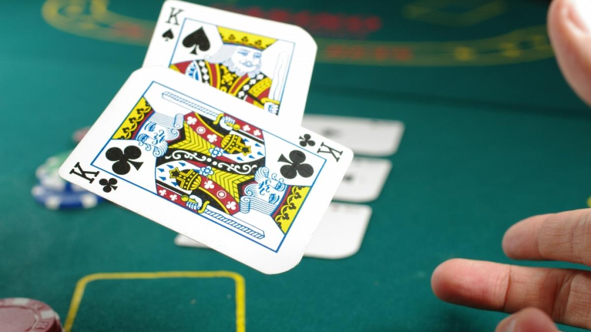 Ein Spieler wirft zwei Spielkarten &uuml;ber den Pokertisch (Foto)