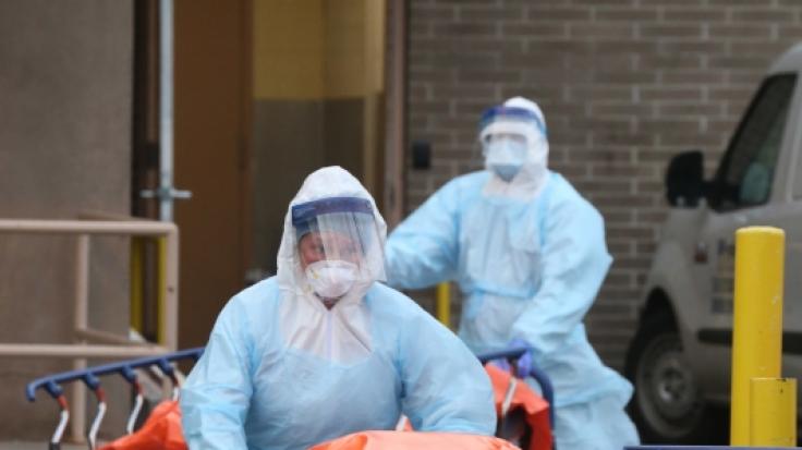 New Yorker Krankenhausmitarbeiter in Schutzkleidung schieben Tragen mit kürzlich Verstorbenen Opfern der Covid-19-Erkrankung aus dem Krankenhaus.