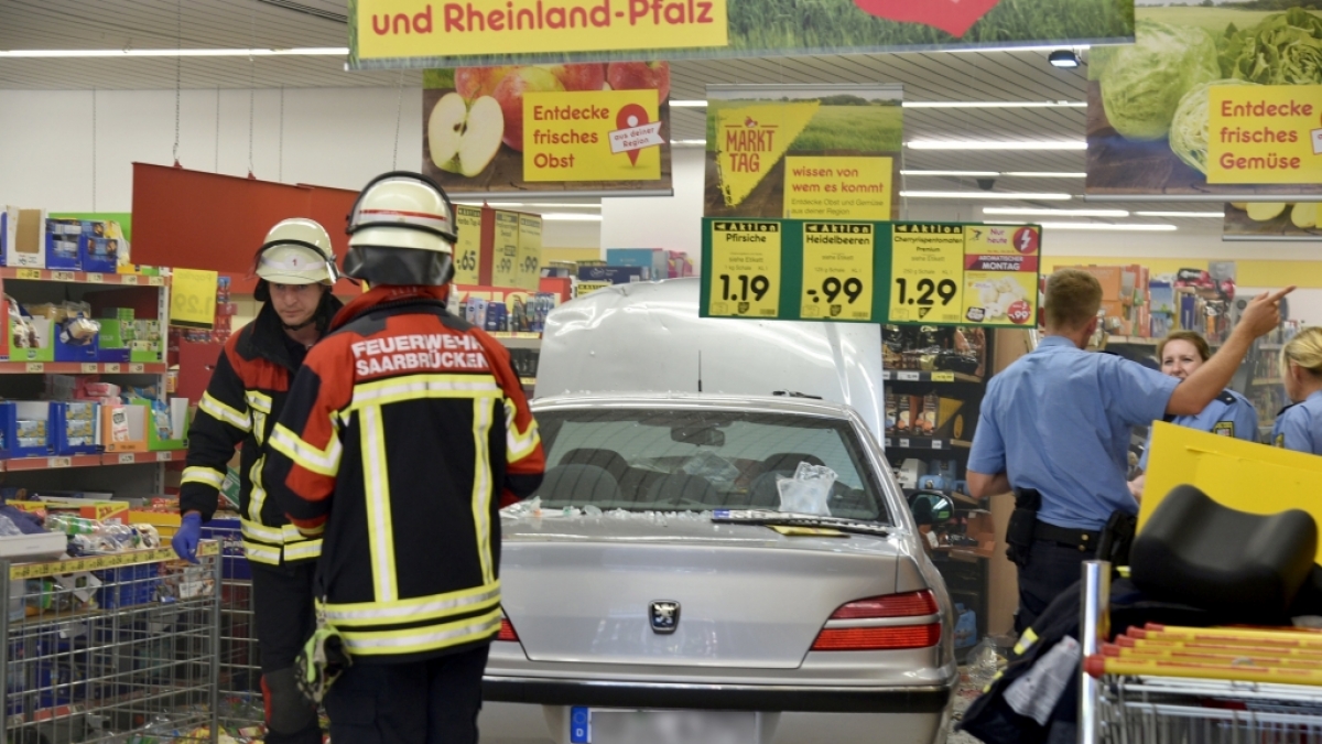 Feuerwehrleute und Polizeibeamte stehen in einem Supermarkt neben einem Pkw, der zuvor in den Supermarkt gefahren war und dabei f&uuml;nf Menschen verletzt hat. (Foto)