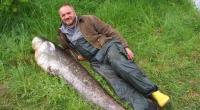 Der Angler Peter Mayer liegt neben einem von ihm geangelten Wels.