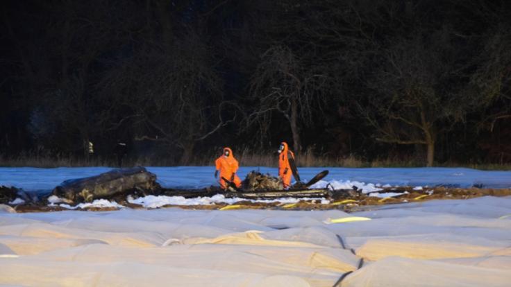 Feuerwehrleute in Schutzanzügen halten Brandwache nach dem Absturz eines Kleinflugzeugs auf einem Spargelfeld im hessischen Erzhausen.