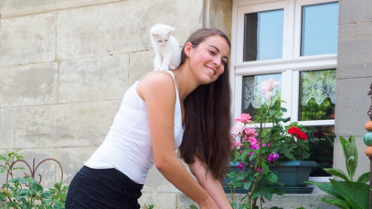 Barbara gießt für den Jungbauernkalender 2018 mit einem Katzenbaby auf der Schulter die Blumen.
