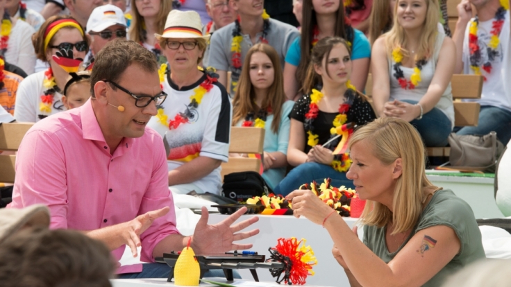 Martin Leutke und Andrea Kiewel testen WM-Gadgets.