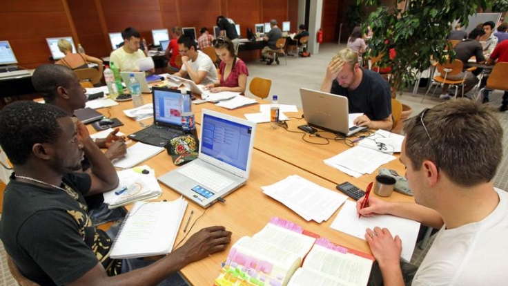 Studenten sitzen in der Bibliothek an Hausarbeiten. Diese sind gar nicht so schwer, wenn ein paar Regeln beachtet werden.
