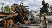 Ein ukrainischer Soldat steht neben einem zerstörten russischen Panzer.