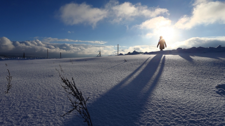 Eine Spaziergängerin läuft im Sonnenschein durch die tief verschneite Landschaft bei Scheidegg (Bayern).