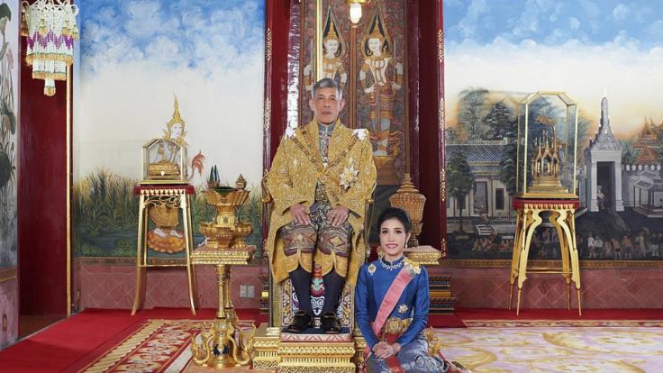 König Maha Vajiralongkorn von Thailand sitzt auf seinem Thron, während neben ihm Sineenat Wongvajirapakdi kniet.